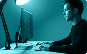 Man at a desk in a dark office reading text on a computer monitor, NIST SP 800-171 Rev 3